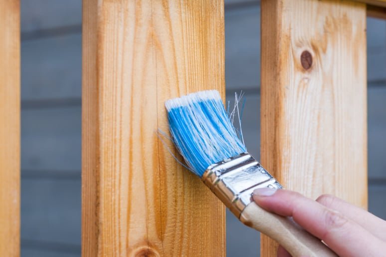 close up of a wooden fence being stained by a paint brush held by a man