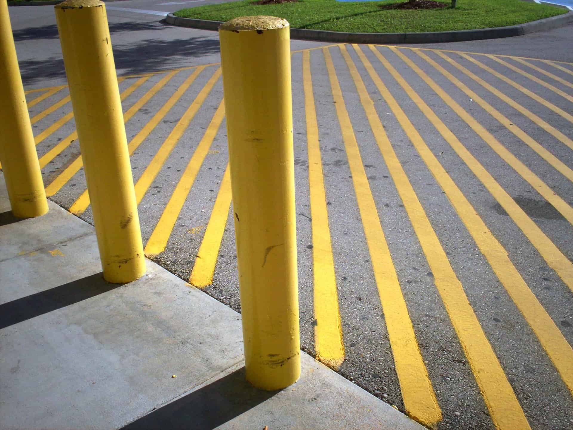 yellow painted lines on concrete in a parking lot with a sidewalk with yellow painted cement posts